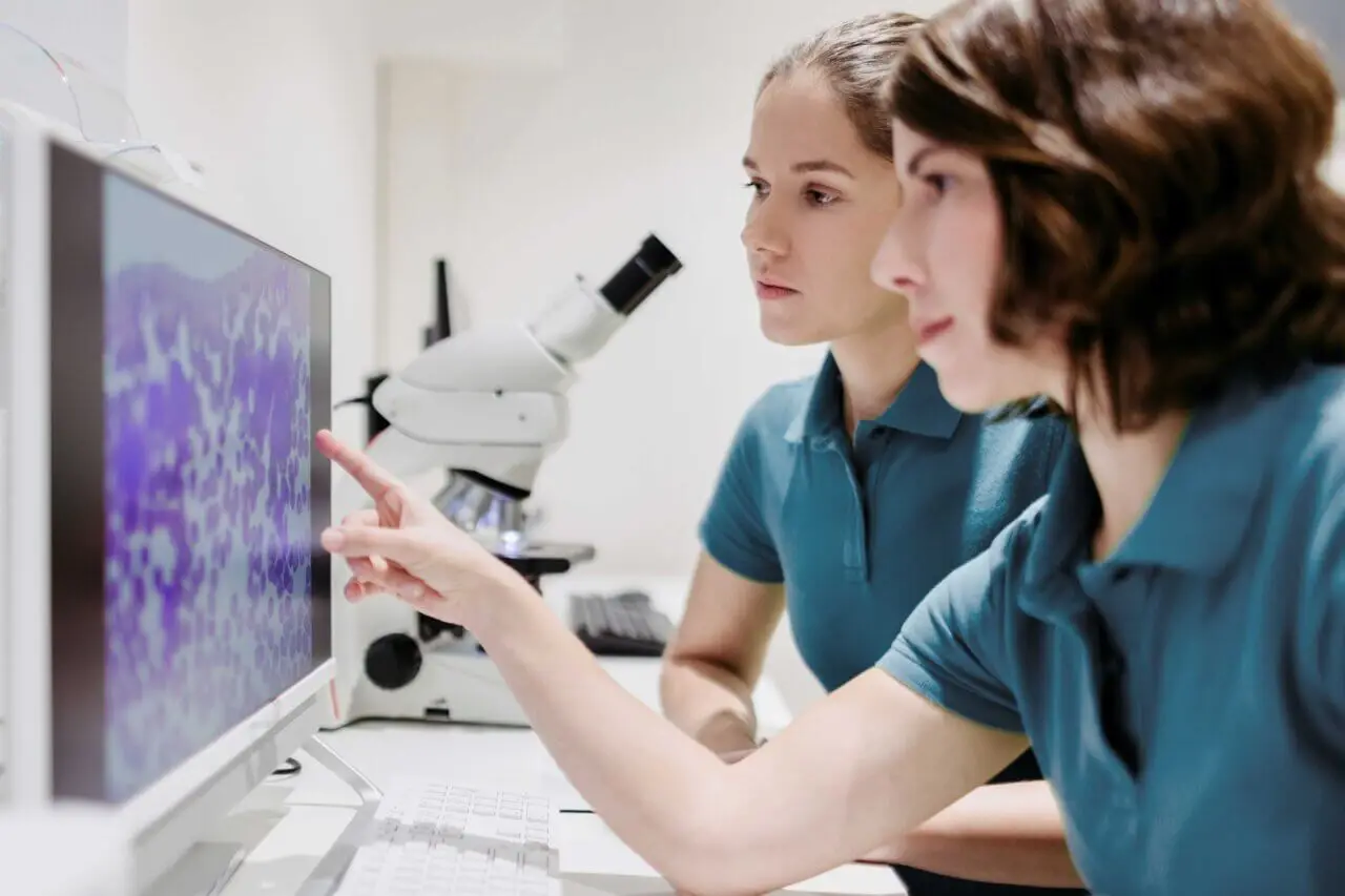 Zwei Personen in medizinischer Schutzkleidung und weißen Handschuhen halten ein Endoskop, während auf einem Monitor im Hintergrund eine innere Aufnahme zu sehen ist.