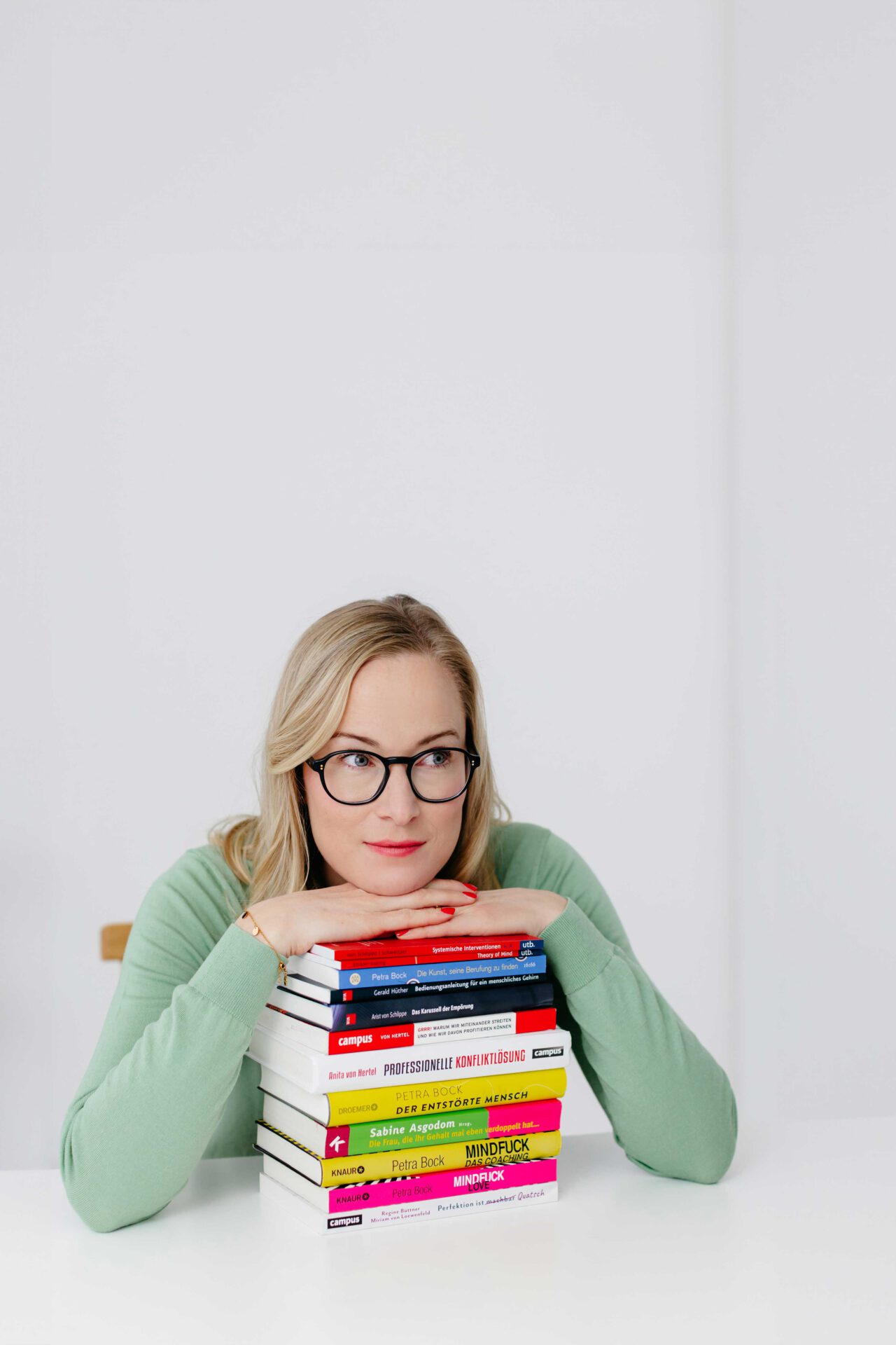 Junge Unternehmerin mit Brille lehnt entspannt auf einem Stapel Fachbücher – authentisches Personal Branding Portrait von Barbara Meyer-Selinger, RAUMFOTOGRAFIN München.