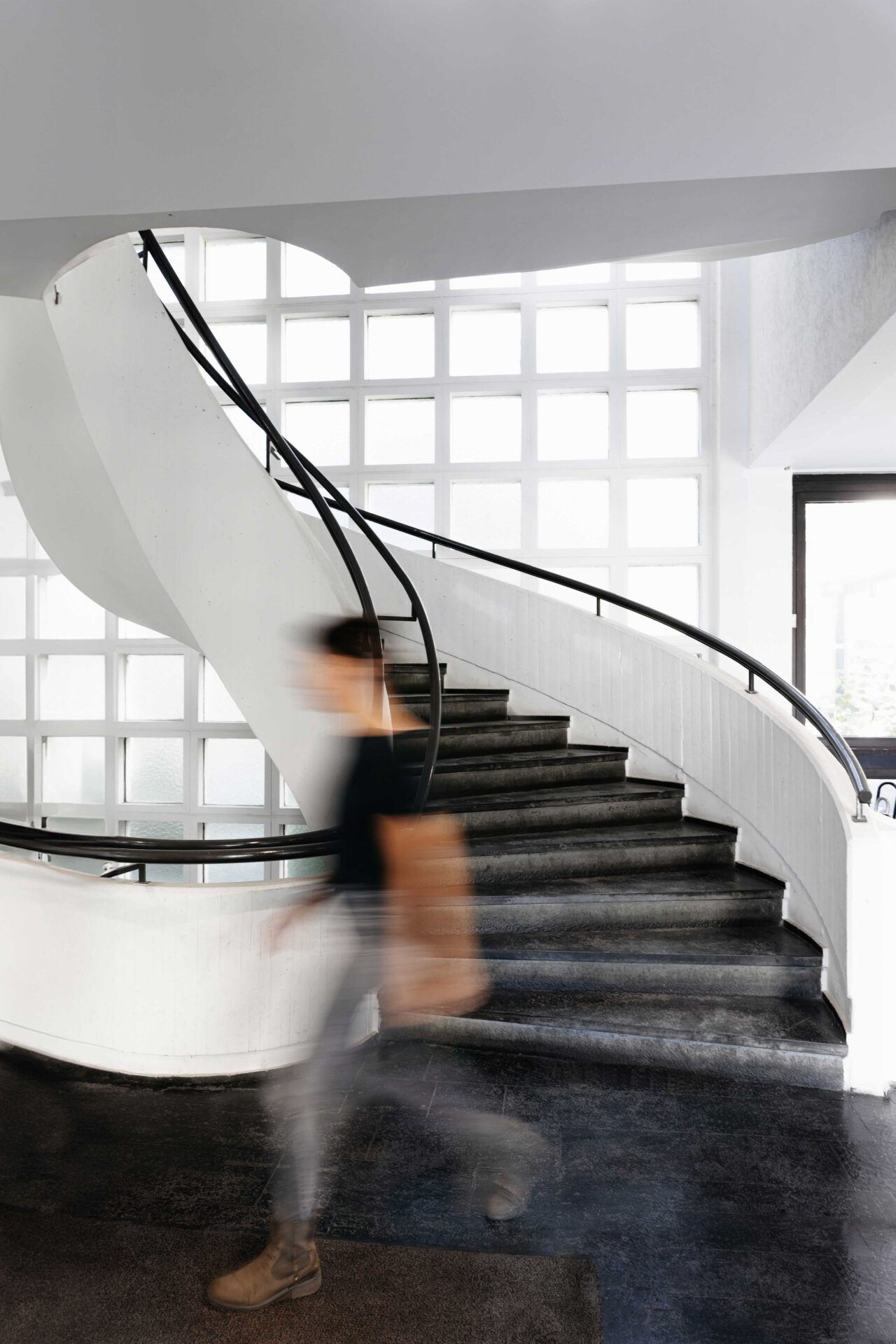 Person in Bewegung auf einer modernen weißen Treppe mit Glasbausteinen im Hintergrund – Branding Foto von Barbara Meyer-Selinger, RAUMFOTOGRAFIN München.
