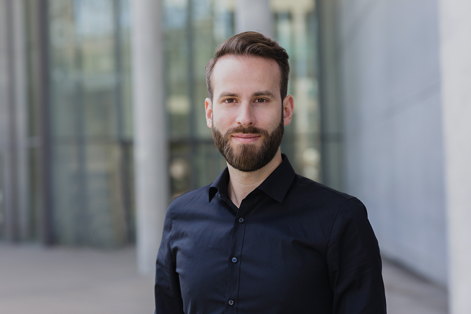 Business Portrait eines Mannes mit Bart in schwarzem Hemd vor moderner Glasarchitektur, Personal Branding Fotografie