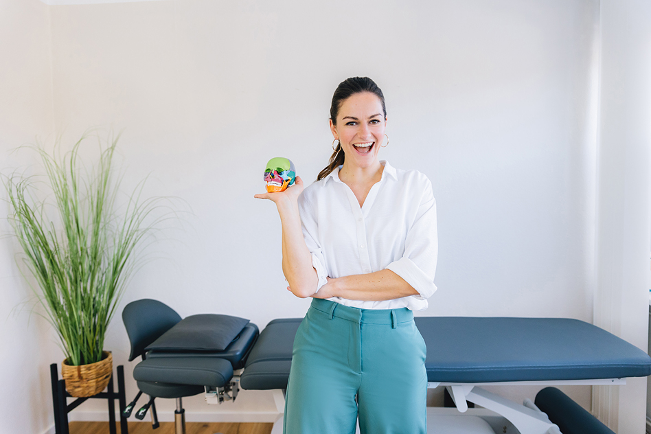 Personal Branding Fotografie einer Therapeutin mit anatomischem Schädelmodell und offener, fröhlicher Ausstrahlung in ihrer Praxis